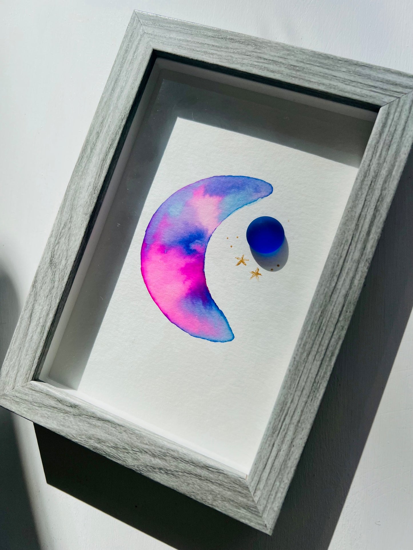 Original sea glass artwork featuring a beautiful watercolor crescent moon and a frosty piece of cobalt blue glass. Artwork is displayed in a 4"x6" shadowbox frame.
