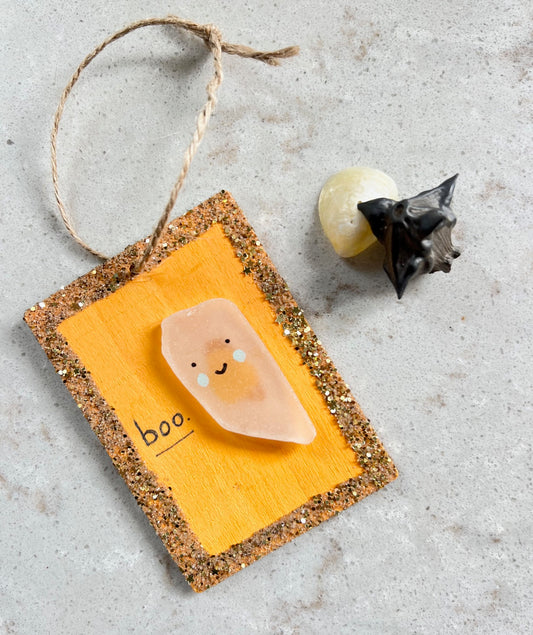 Decorative sign with a cute face design on an orange background, hanging on a textured surface.